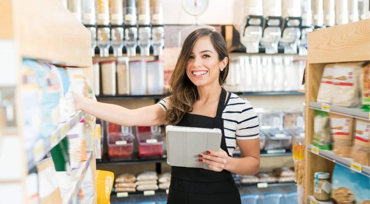 A store employee uses a tablet while organizing product shelves, illustrating inventory management for demand and supply planning.